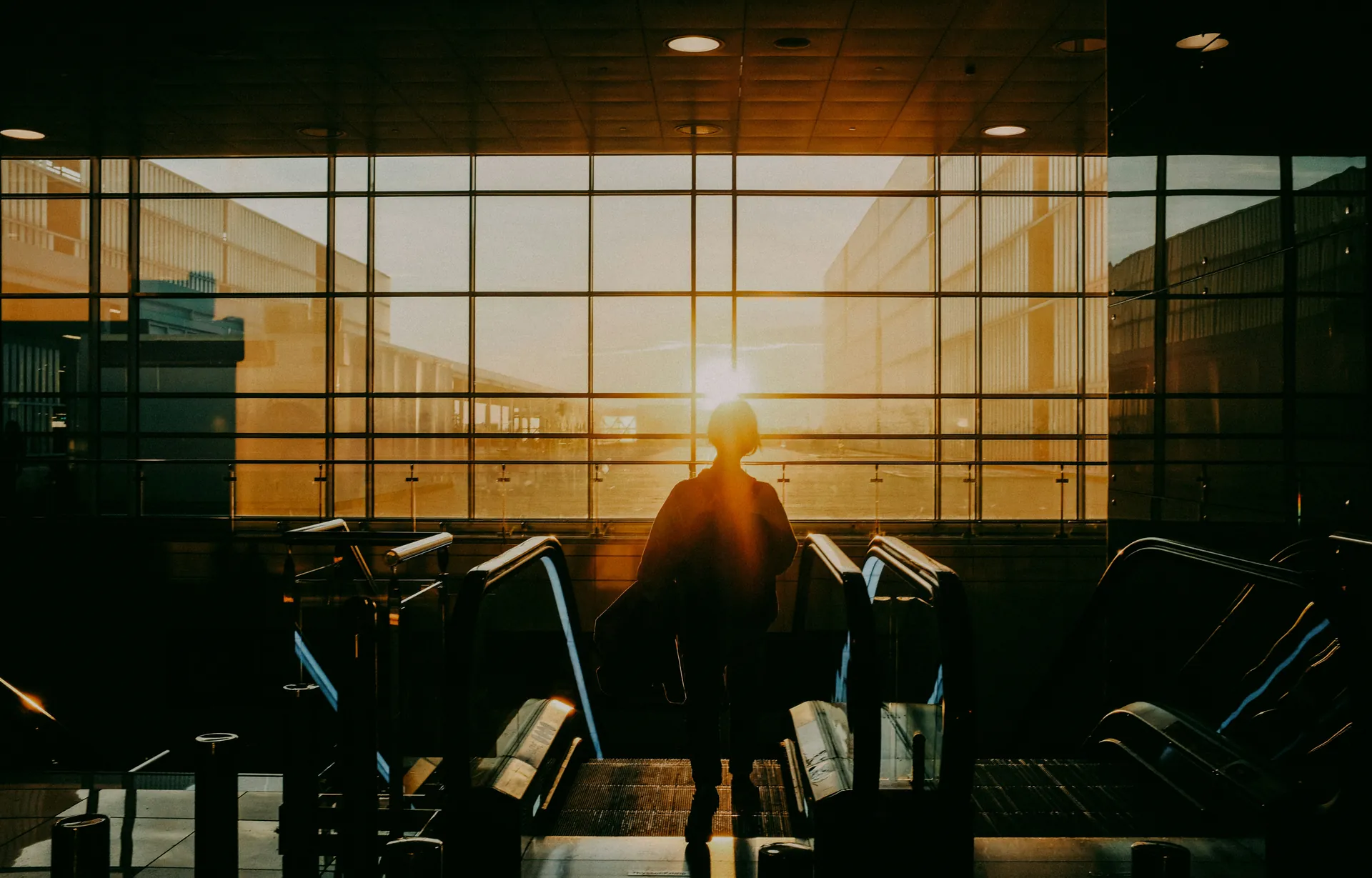 A traveller rides the escalator towards a terminal window at sunset